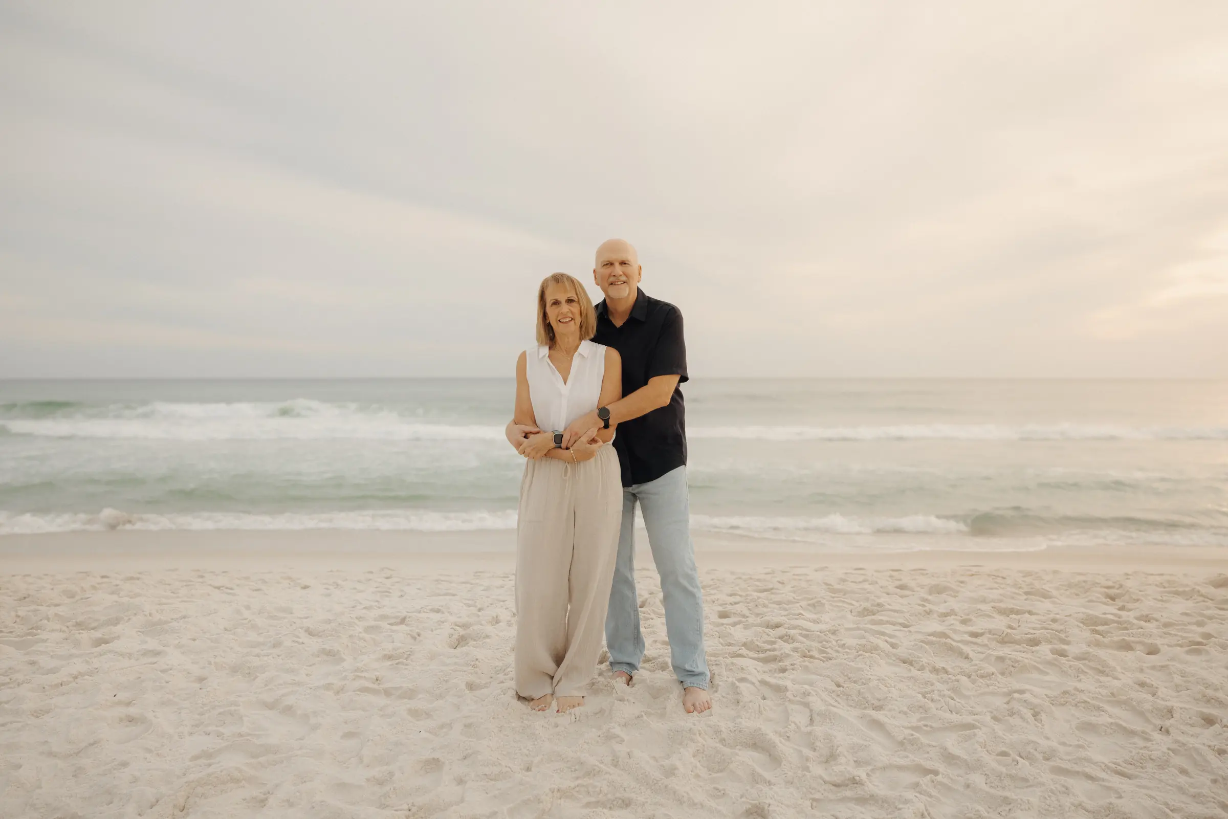 Couple standing on white sand at the Gulf's edge in soft evening light